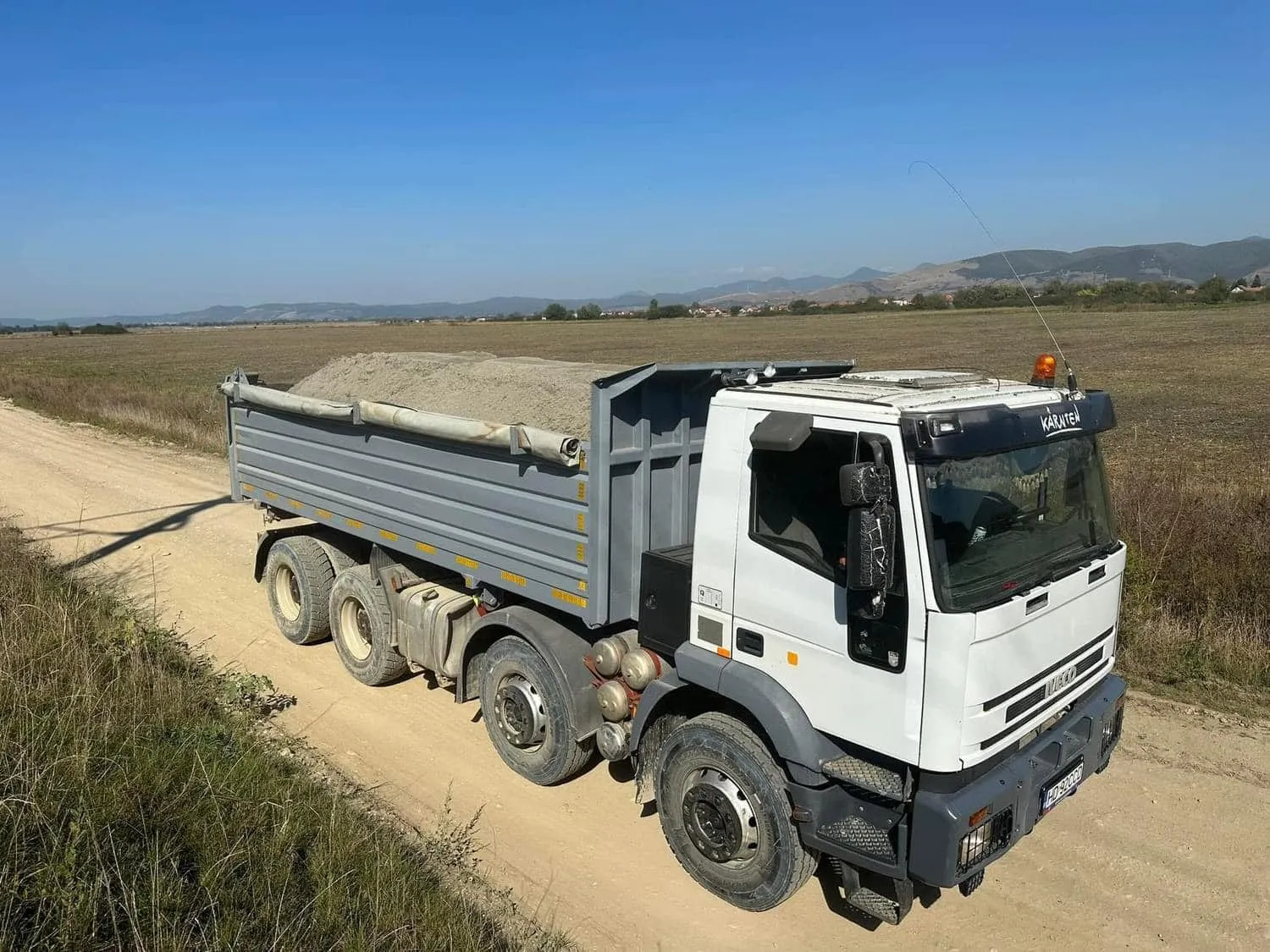 Basculantă 8x4 încărcată, pe un drum de câmp